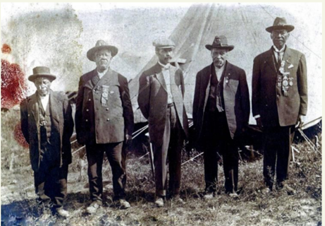 Photo of Benjamin Franklin Jennings standing outside a home, holding a fence with his hat in the other hand