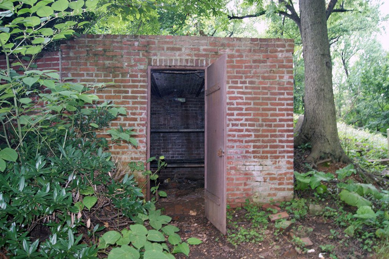 Photo of cemetery vault with door open, green forest shrubbery surrounds it
